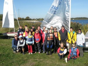 Dieses Bild zeigt eine Gruppe an Seglern, die vor 2 kleinen Segelbooten stehen.